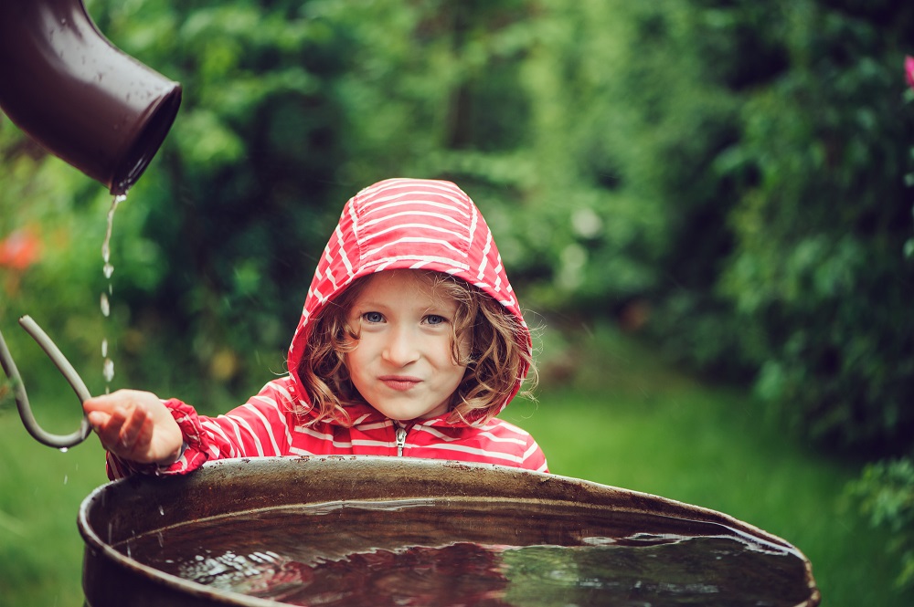 child girl playing with water barrel in rainy summer garden. Water economy and nature care concept